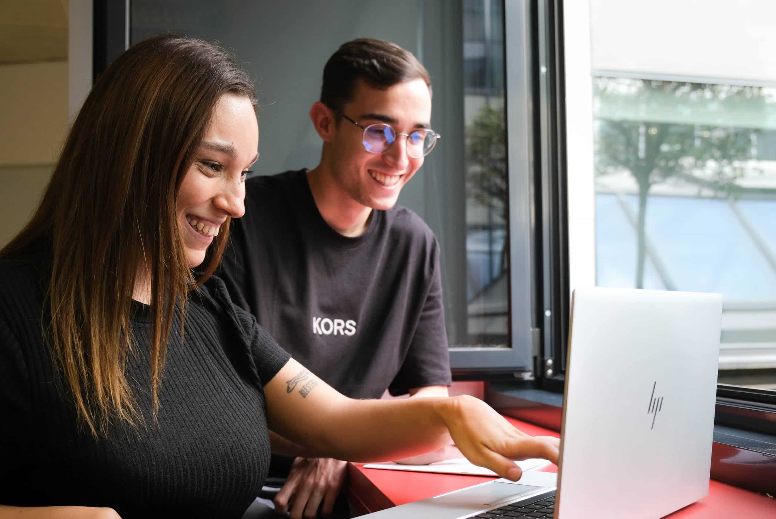 2 people smiling and looking at the computer at ERNI Spain offices.