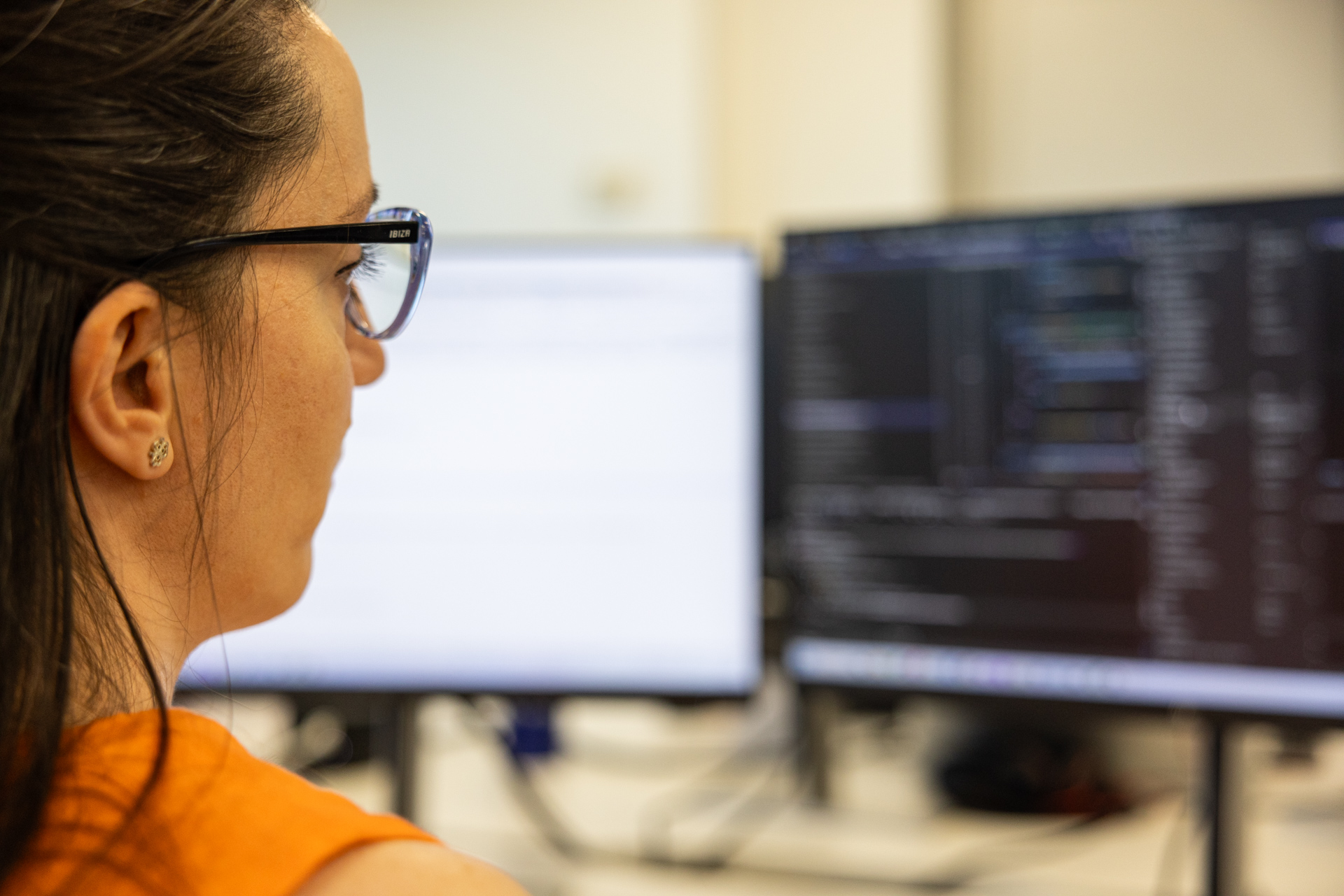 A young woman sitting at a desk, illuminated by her laptop screen, surrounded by lines of computer code and abstract AI graphics, symbolising the intersection of human responsibility and generative AI systems.