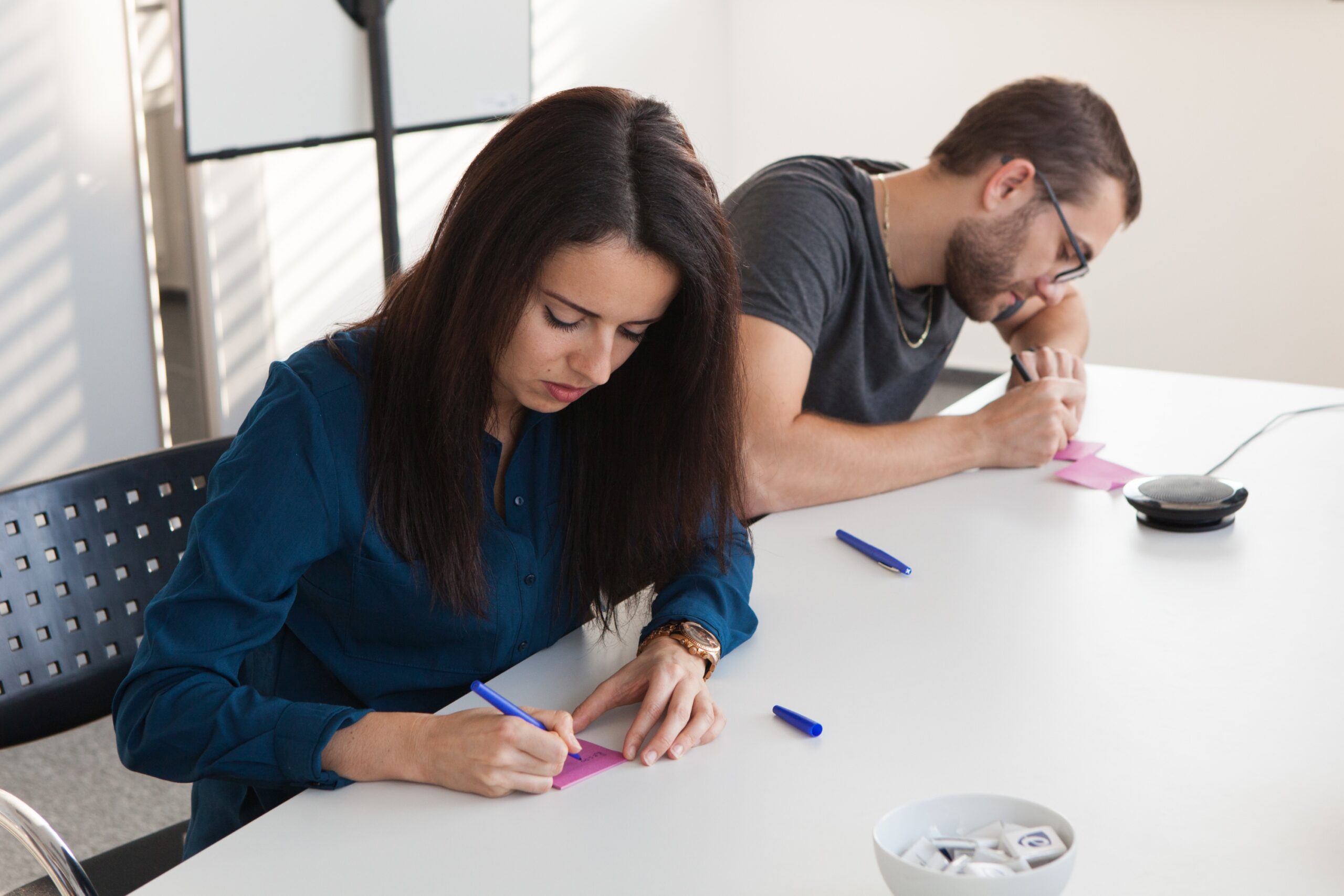 Two colleagues writing ideas on colourful post-its during a scrum session, collaborating to improve team agility and workflows.